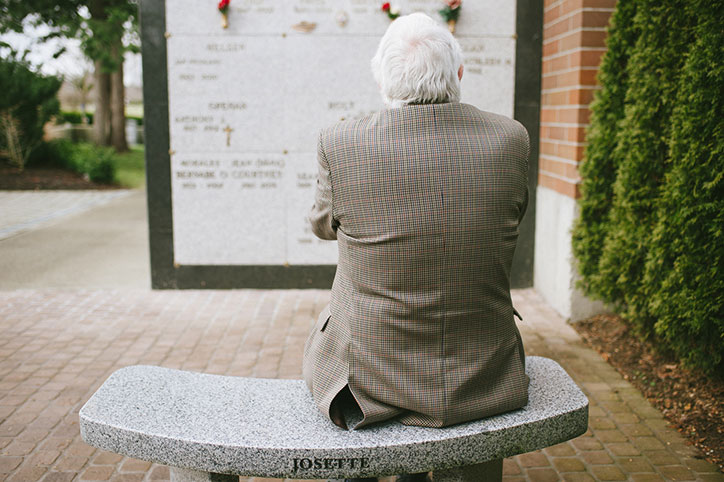 white haired man on bench near cremation niches